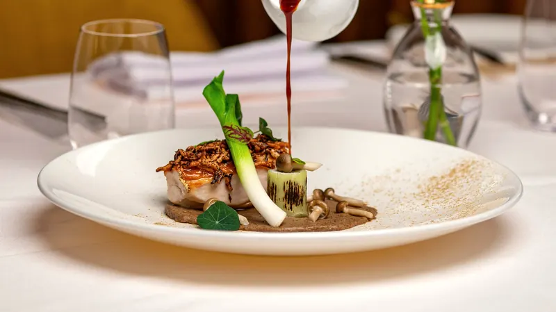 Assiette de poisson, poireau grillé et champignons, nappée d'un jus versé au pichet